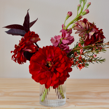 A bold and modern arrangement featuring red zinnias, pink stock, and burgundy accents. This striking bouquet in a textured glass vase is perfect for birthdays, anniversaries, or to make a statement. Available for local delivery in Wake Forest, NC.