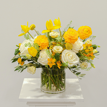 A bright and cheery flower arrangement with yellow tulips, ranunculus, and white roses in a clear glass vase. This sunny bouquet is perfect for birthdays, congratulations, or to simply brighten someone's day. Available for local delivery in Wake Forest, NC.