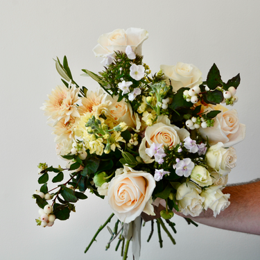 A hand-tied bouquet featuring creamy white and peach roses, accented with delicate fillers and greenery. This elegant wrapped bouquet is perfect for birthdays, anniversaries, or to express your congratulations. Available for local delivery in Wake Forest, NC.