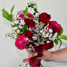 A richly colored, hand-tied bouquet featuring deep red roses, carnations, and zinnias, accented with purple phlox and delicate fillers. This romantic bouquet is perfect for anniversaries or to express sympathy and condolences. Available for local delivery in Wake Forest, NC.
