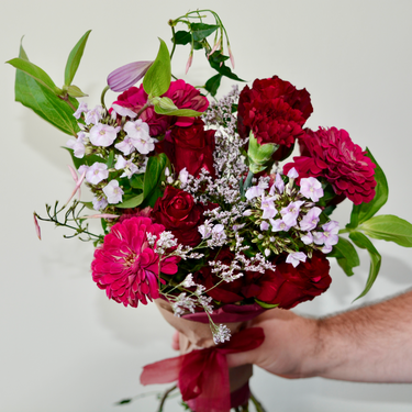 A richly colored, hand-tied bouquet featuring deep red roses, carnations, and zinnias, accented with purple phlox and delicate fillers. This romantic bouquet is perfect for anniversaries or to express sympathy and condolences. Available for local delivery in Wake Forest, NC.