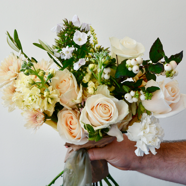 A hand-tied bouquet featuring creamy white and peach roses, accented with delicate fillers and greenery. This elegant wrapped bouquet is perfect for birthdays, anniversaries, or to express your congratulations. Available for local delivery in Wake Forest, NC.