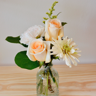 A sweet and simple arrangement with peach roses, white carnations, and a pale green chrysanthemum. This petite bouquet in a decorative glass vase is perfect for a new baby, thinking of you, or as a small gesture of appreciation. Available for local delivery in Wake Forest, NC.