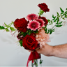 "A hand-tied bouquet featuring deep red roses, pink gerbera daisies, and carnations, accented with a peach chrysanthemum and greenery. This romantic bouquet is perfect for anniversaries or to express sympathy. Available for local delivery in Wake Forest, NC.