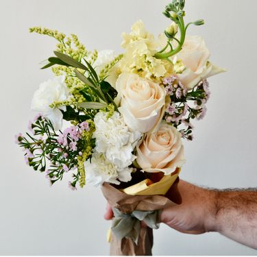 A hand-tied bouquet with peach roses and white carnations, accented with delicate fillers and greenery. This elegant wrapped bouquet is perfect for birthdays, anniversaries, or to express your congratulations. Available for local delivery in Wake Forest, NC.